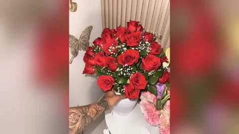 Vibrant bouquet of fresh red roses in a white vase against a neutral wall background.