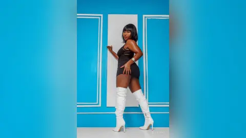 Stylish woman in a black mini dress and white knee-high boots posing against a bright blue studio background.