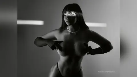 Black and white silhouette of a woman in a pearl necklace posing in moody studio lighting.
