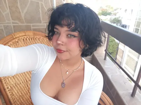 Smiling woman with short dark hair in a white top sitting on a sunny balcony.