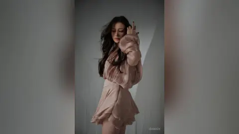 Elegant woman in a flowing blush pink dress posing gracefully in a minimalist studio setting.