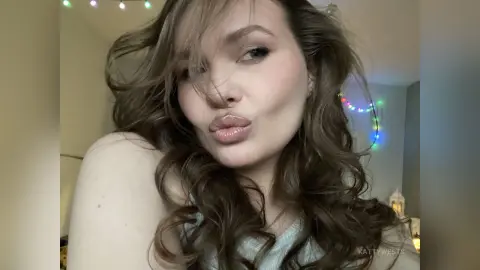 Blonde woman in a light blue top making a playful pouty face in a cozy indoor setting.
