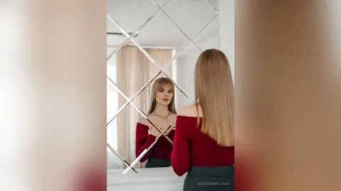 Elegant woman in a red off-the-shoulder top looking into a geometric mirror in a bright, modern room.