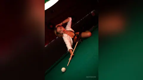 Glamorous woman in a white shirt and black lingerie playing pool in a moody, dimly lit billiards room.