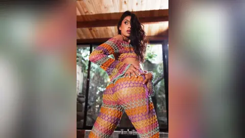 LucyMartin poses in a colorful, patterned mesh crop top and matching leggings, looking over her shoulder with long wavy hair.