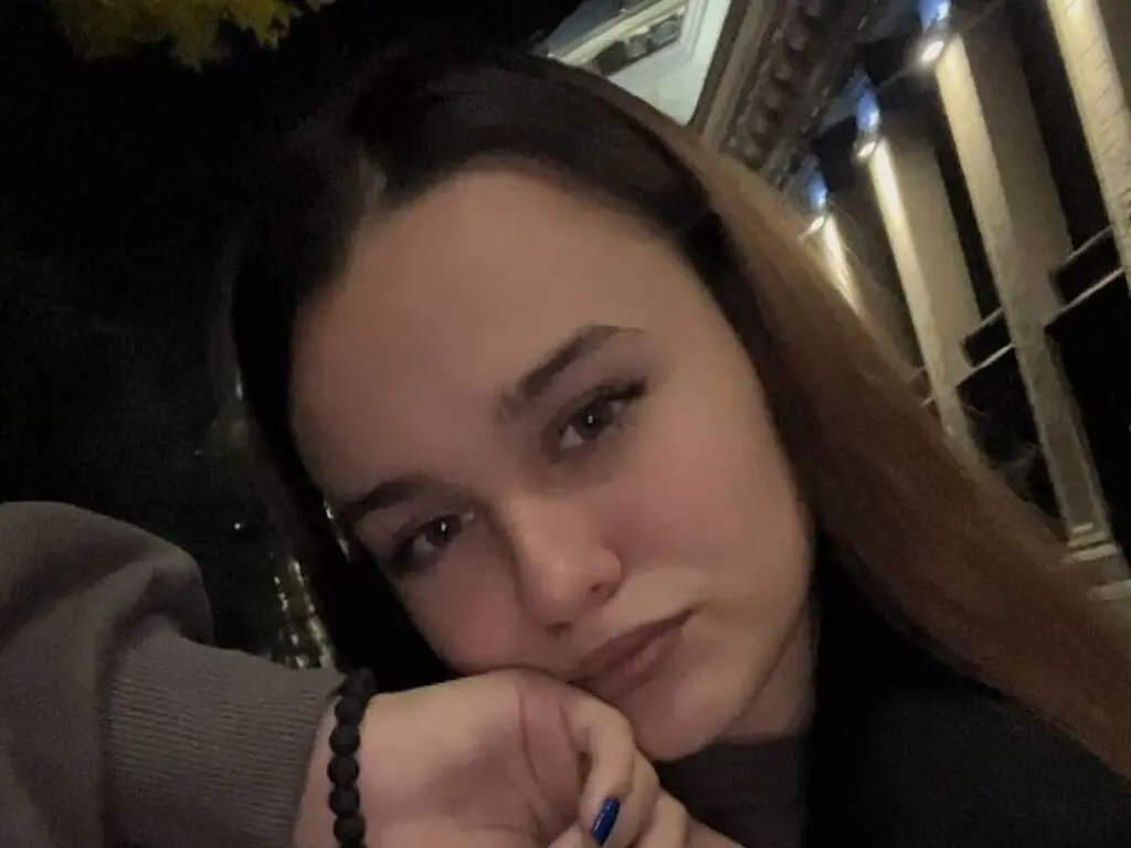 Young woman in a cozy grey sweater posing for a nighttime selfie in front of classical architecture.