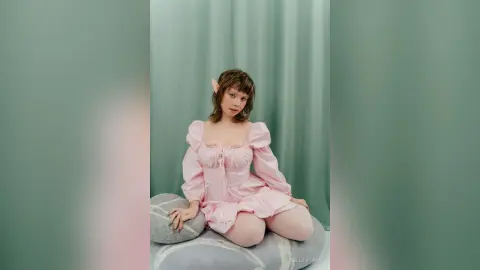 Ethereal elf woman in a romantic pink puff-sleeve dress sitting against a soft mint green backdrop.