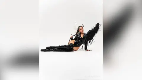 Model in a black latex bodysuit with large black wings posing against a white background in a dramatic mood.