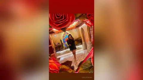 Stylish woman in a black mini dress posing in a luxury Mediterranean villa with floral decor.