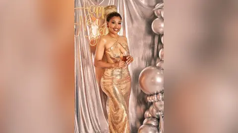 Smiling woman in a glamorous gold sequin gown celebrating New Year's Eve with champagne in a festive setting.