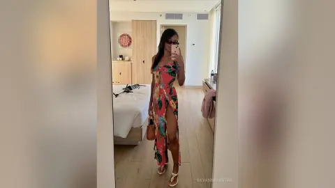 Stylish woman in a floral maxi dress posing in a modern bedroom mirror for a summer fashion look.