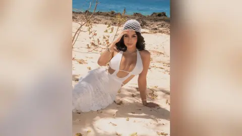Elegant woman in a white lace beach outfit posing on a sunny tropical sand beach.