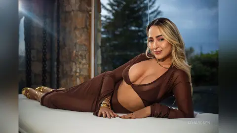 Smiling blonde woman in a brown cutout maxi dress lounging on a white sofa in a modern stone interior.