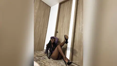 Stylish woman in a purple bodysuit and black heels sitting on a marble floor in a modern minimalist room.