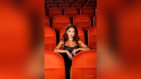 Elegant woman in a black cocktail dress sitting in red theater seats with a glamorous mood.