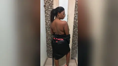 NahomyBrown poses with her back turned, wearing a black satin robe that slips down to show her bare back and shoulders.