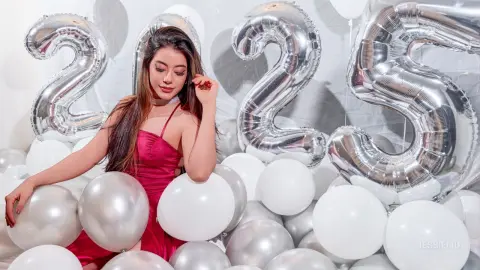 JessieLiu poses in a red satin dress while surrounded by white and silver balloons.