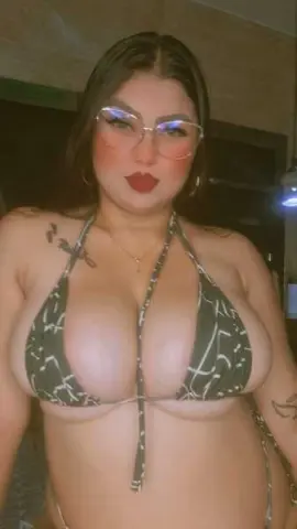 Woman in a patterned halter bikini top and glasses posing indoors with a confident mood.