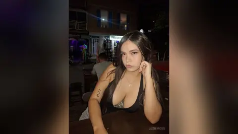 Young woman in a black tank top sitting at an outdoor restaurant table at night.