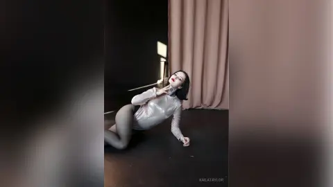 Glamorous woman in a sparkling silver bodysuit posing elegantly in a dark studio setting.