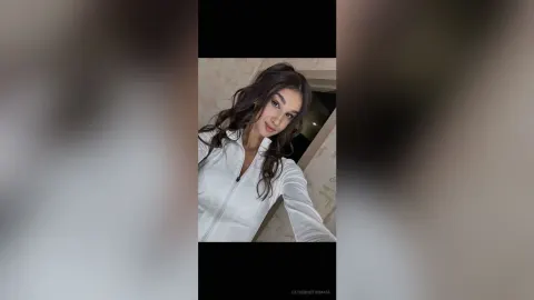 CatherineThomase — CatherineThomase poses in a white long-sleeve top with her wavy brown hair flowing over her shoulders.