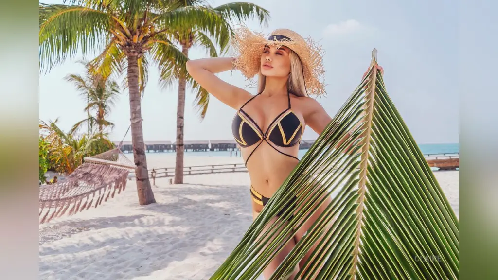 Blonde woman in a beige bikini relaxing in a luxury turquoise swimming pool by the ocean.