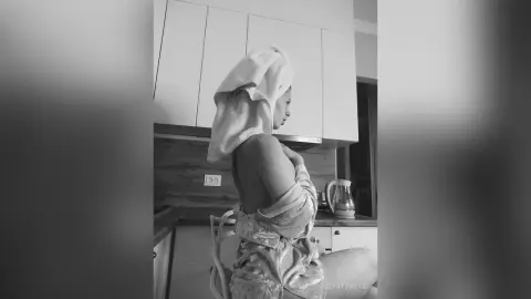 RubyAttwood stands in a kitchen wearing a light-colored towel wrapped around her head and a patterned towel wrapped around her chest.