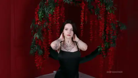 Young woman in a black satin dress posing against a romantic red floral backdrop with hanging red flowers.