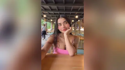 Smiling young woman in a pink tank top relaxing at an outdoor wooden patio restaurant.