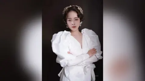 Elegant woman in a white puff-sleeve gown and gold headband posing gracefully against a dark studio background.