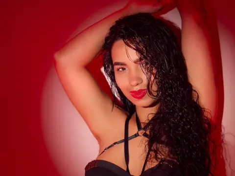 Glamorous woman with curly hair in a black strappy top posing against a moody red studio background.