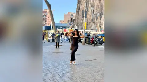 Stylish woman in a sleek black maxi dress posing on a sunny city street near historic architecture.