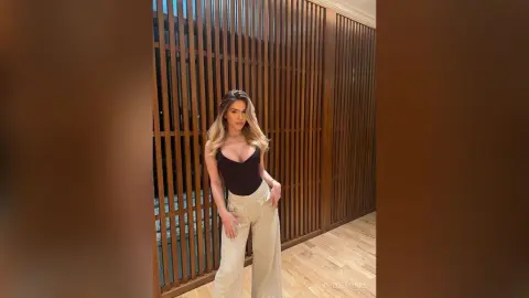 Elegant woman in a black bodysuit and glittery wide-leg trousers posing against a modern wooden slat wall.