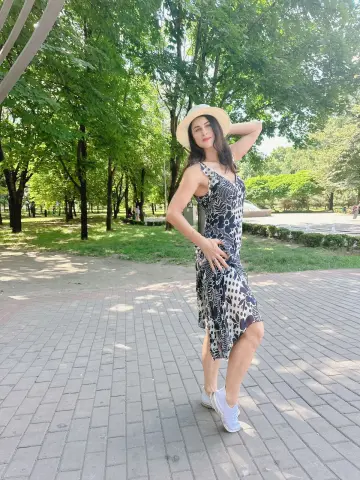Woman in a floral black midi dress and white sneakers posing in a sunny green park.