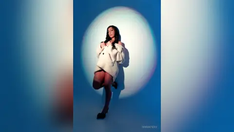 Stylish woman in a white fuzzy coat posing against a dreamy blue circular light backdrop.