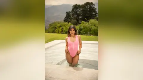 Woman in a pink one-piece swimsuit relaxing in a luxury infinity pool overlooking a scenic mountain landscape.