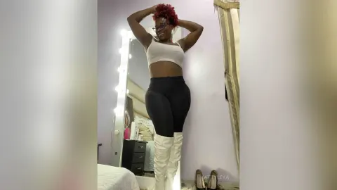 KattyLeya — KattyLeya poses in a white crop top and black leggings with white thigh-high boots in front of a lighted mirror.