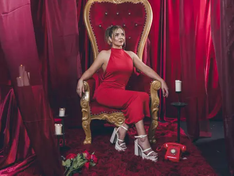 Elegant woman in a red halter jumpsuit sitting on a gold throne amidst luxurious red velvet curtains.