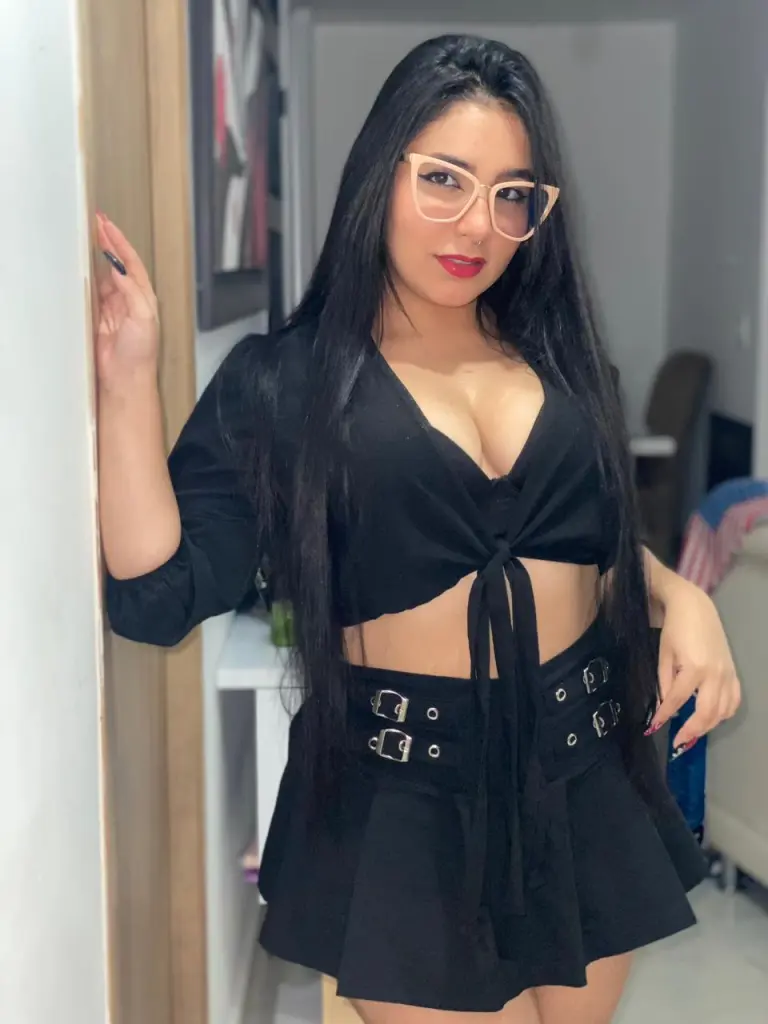 ViolettaBlacke with long dark hair and glasses poses topless, showing her tattoos and cleavage while holding her breasts.