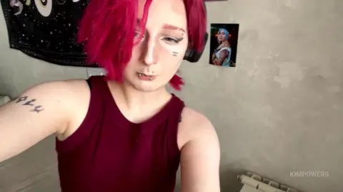 Woman with pink hair and maroon tank top in a casual indoor setting.
