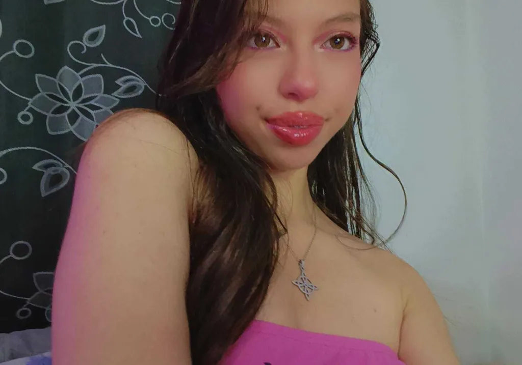 AmmelieJoy poses in a black strap bra, looking over her shoulder with her hand near her face.