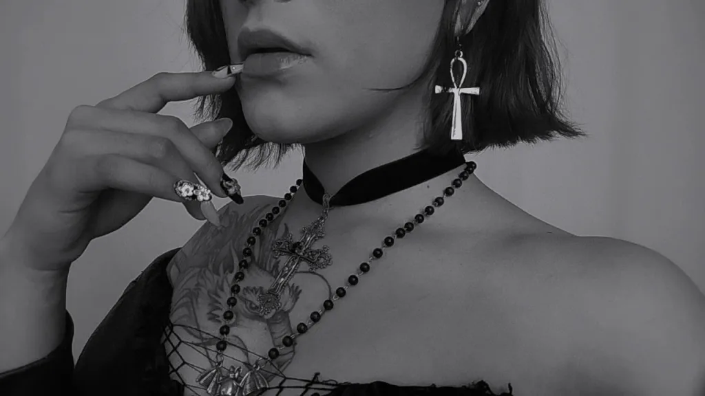 SarahHiill with red hair and heavy eyeliner poses in black fishnet clothing and a black choker.
