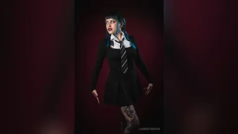 Gothic woman in a black schoolgirl outfit and tie posing against a dark moody background.