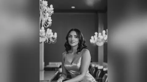 Elegant woman in a shimmering satin dress posing in a sophisticated, moody black and white interior setting.