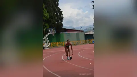 Athletic woman in sports bra training on an outdoor red running track under a cloudy sky.