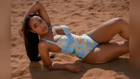 Beautiful woman in a light blue patterned swimsuit relaxing on a sunny sand beach.