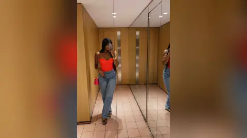 Young woman in a red tank top and blue jeans taking a mirror selfie in a modern elevator.