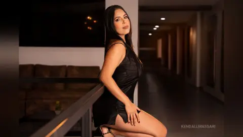 Elegant woman in a black satin dress posing in a modern dimly lit hallway.