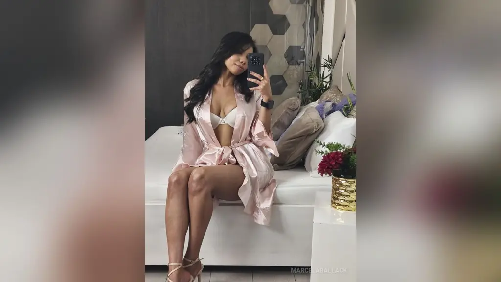 MarcelaBallack — Woman in a pink silk robe sitting on a white bed in a bright, modern bedroom.