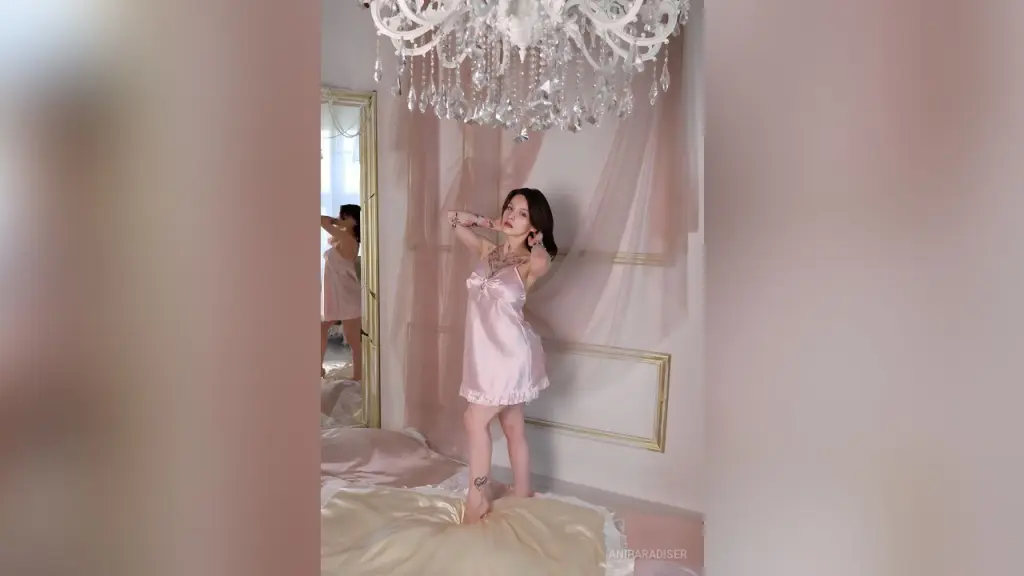 AniParadiser — AniParadiser stands in a pink satin slip dress under a crystal chandelier.